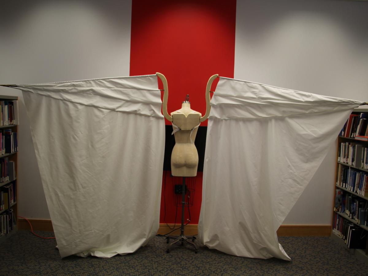 Bennett's costume of wings shorn of feathers. A dress form in the center of two sheets on its left and right, mimicking wings outstretched.