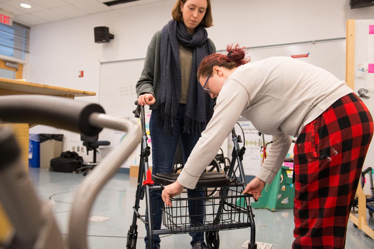 A photo of two young women in a classroom working to modify a walker