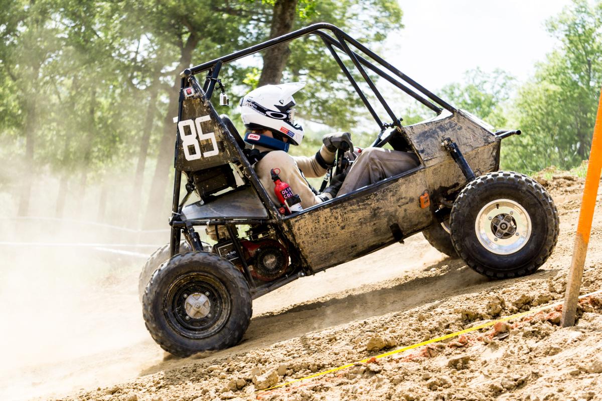 A photo of a person driving a baja vehicle on a dirt track