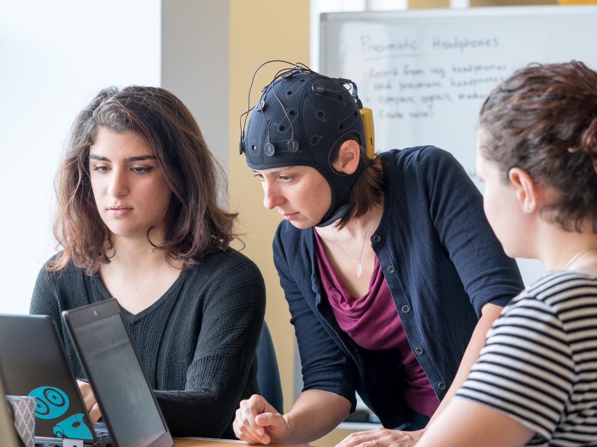 A photo of three people looking at a computer on a desk as part of their human augmentation research