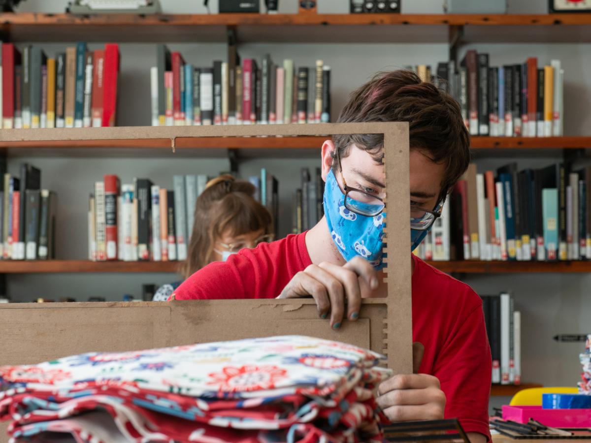 A student in red shirt works on a wooden loom in the Library.