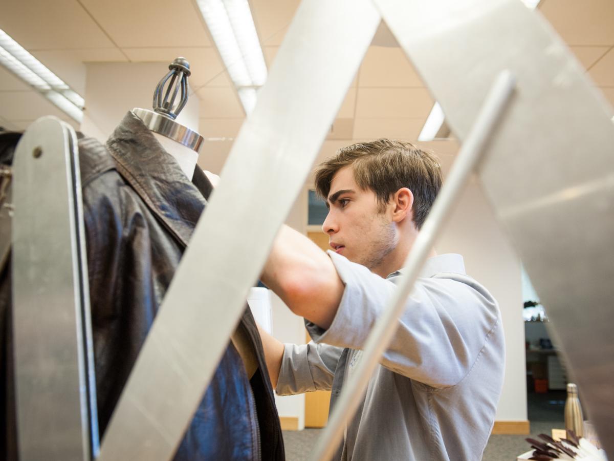 Bennett Taylor '22 looks over a leather bomber jacket that he designed as part of a special collaboration with Tom Pearson, Olin's Sketch Model Creative-In-Reference for academic year 2019 - 2020. A man looks at leather bomber jacket on a dress form.