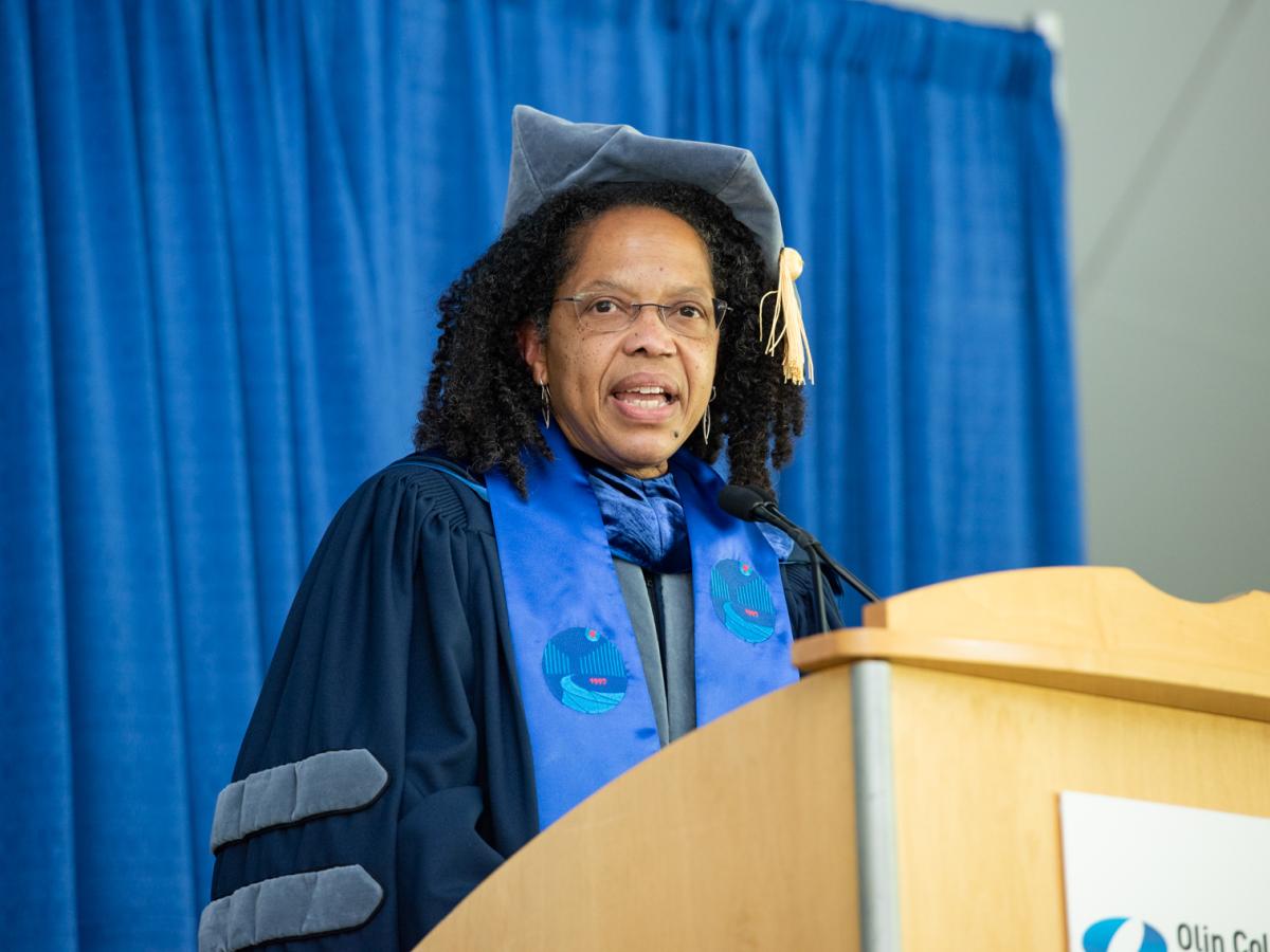 President Gilda Barabino, in blue cap and gown, stands at a podium and addresses the Class of 2021 and their families, faculty, staff and guests at Olin Commencement. 