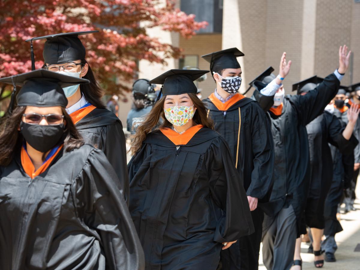 A line of students in cap and gown wave and process down to the Olin Commencement Tent.