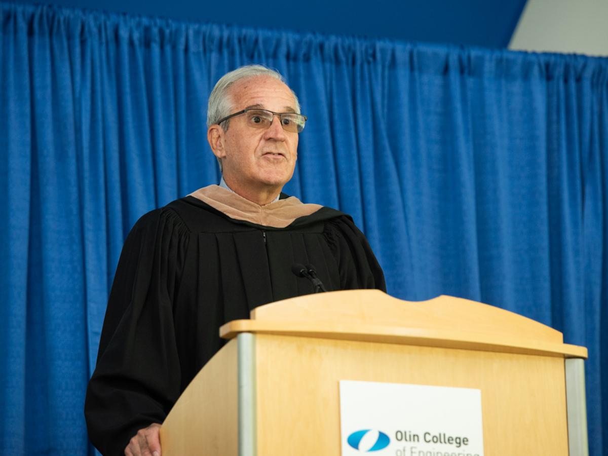 Ken Stokes, Olin College Chair of the Board of Trustees stands at a podium and offers the Commencement Greetings