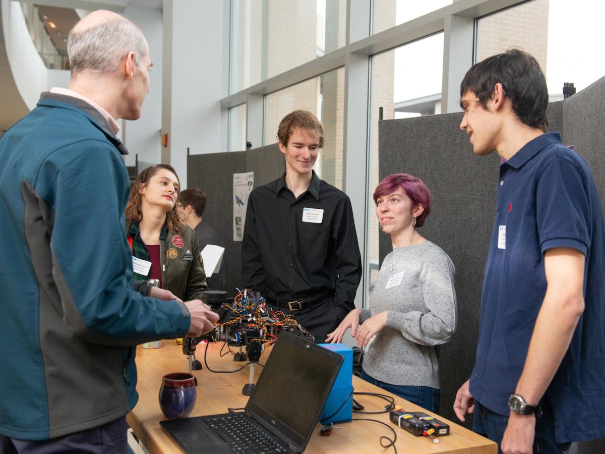 Three students behind a table present their hexapod to another person at Fall Expo 2019