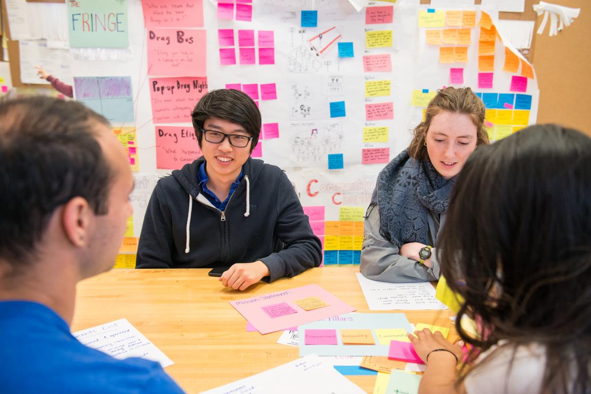 Olin College of Engineering students sitting at a table in a sticky note-filled classroom