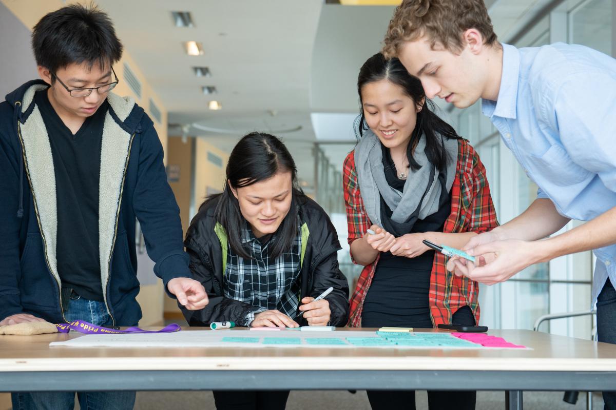 Four members of an Olin SCOPE Team work together on a table