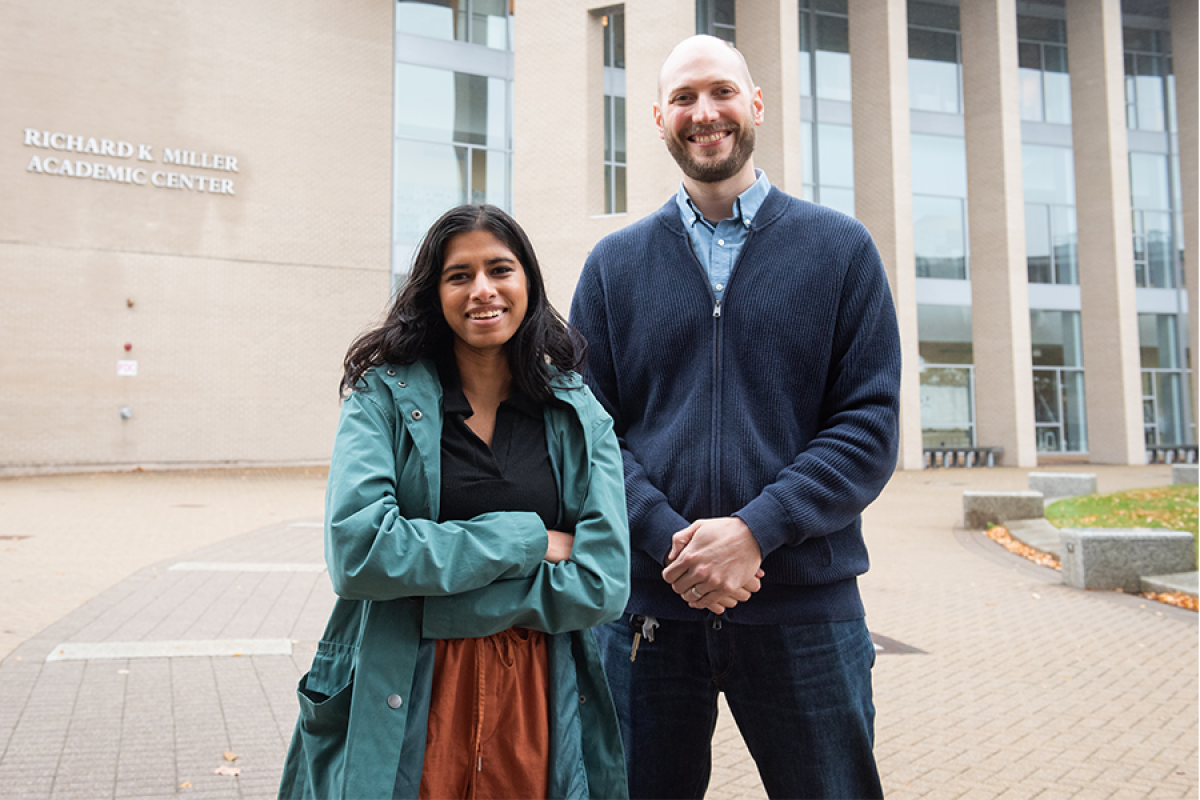 Two people - a student and a professor - stand outside on campus facing the camera head-on