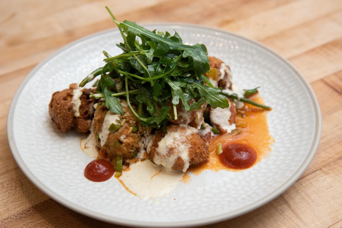 A styled food dish served by Olin Dining as part of Convocation 2021. A white plate dressed with beautifully styled food - greens on top of croquets and a red sauce.