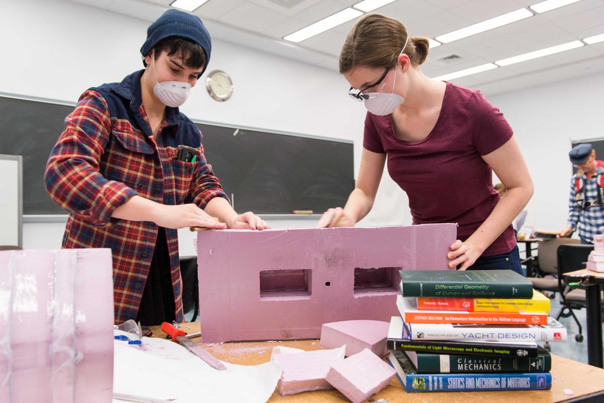 A photo of two students working together to construct a boat prototype