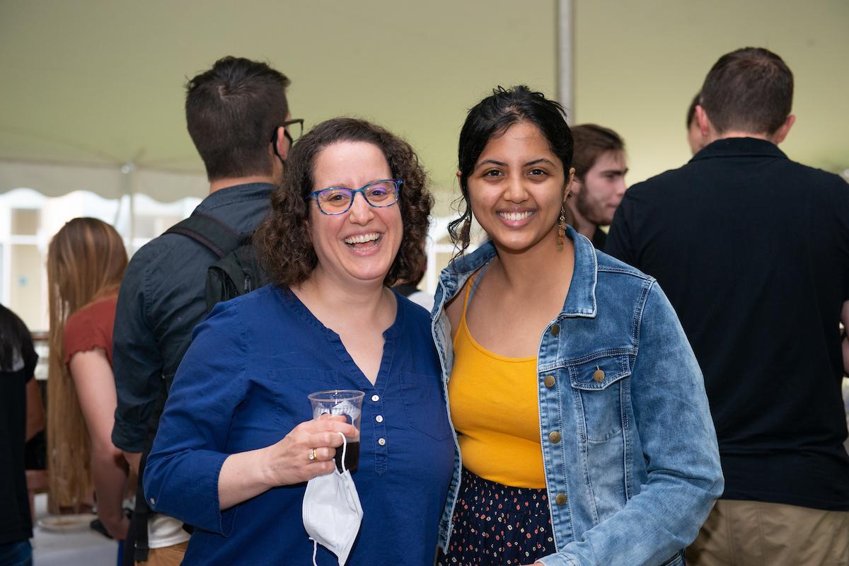 Two people smile for the camera during an outside event under a tent.