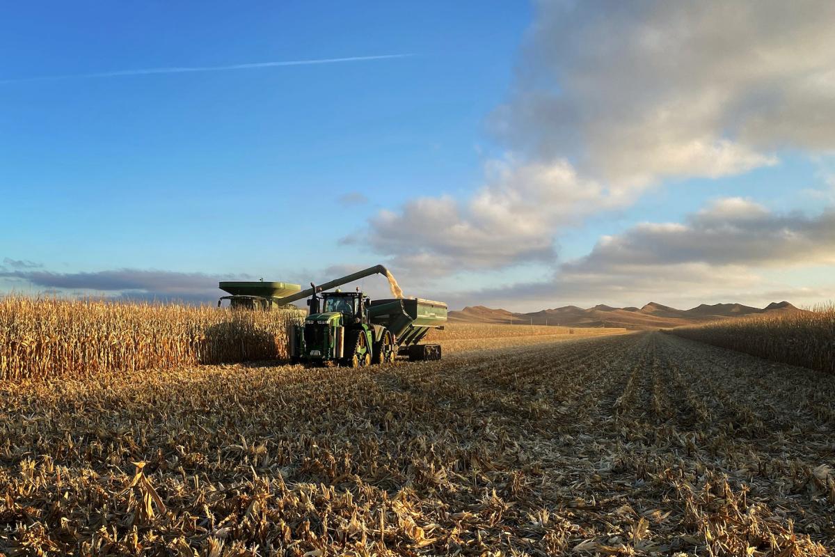 A piece of farming machinery runs in a field draped in shadows and clouds.