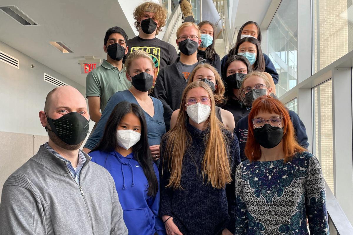 A group of over 10 people wearing masks stand on stairs to take a group photo.