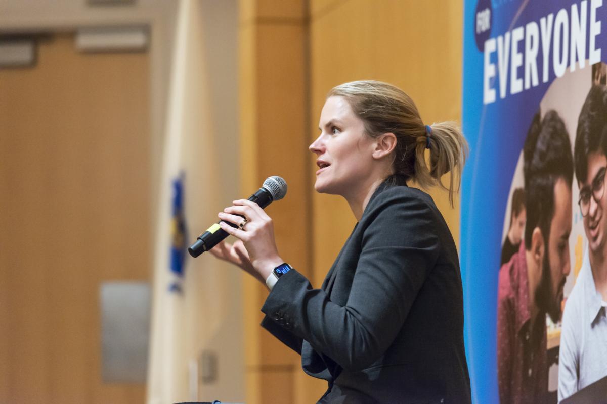Frances Haugen '06, Olin College alumna, holds a mic in front of a crowd in Olin's Norden Auditorium.