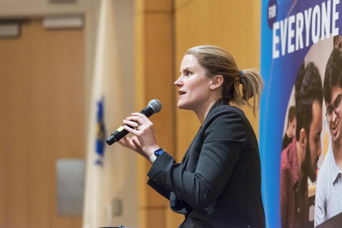 Frances Haugen '06, Olin College alumna, holds a mic in front of a crowd in Olin's Norden Auditorium. Frances Haugen '06, Olin College alumna, holds a mic in front of a crowd in Olin's Norden Auditorium.