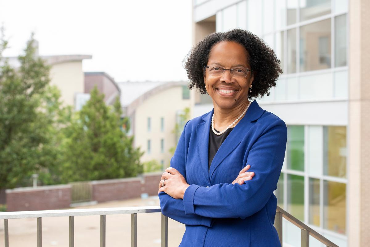 Dr. Gilda A. Barabino, Olin College of Engineering President, smiles and poses outside with trees in background, with arms crossed while wearing a royal blue blazer.