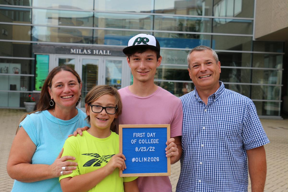 A mother and father pose with their two children in front of a glass building.