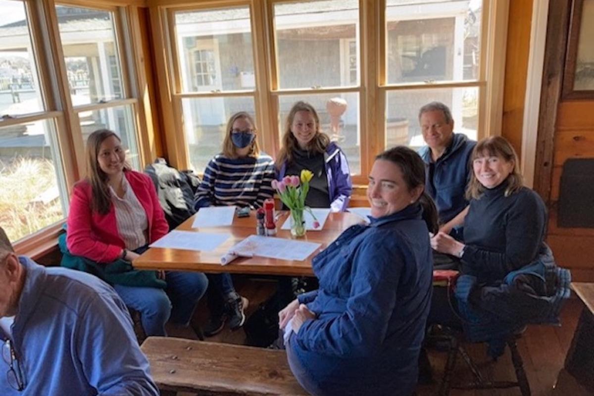 The cross-campus Olin team visits with Eastern Wind Power on Martha’s Vineyard to learn more about the technology. A group of seated people, look at the camera from around a wooden table.