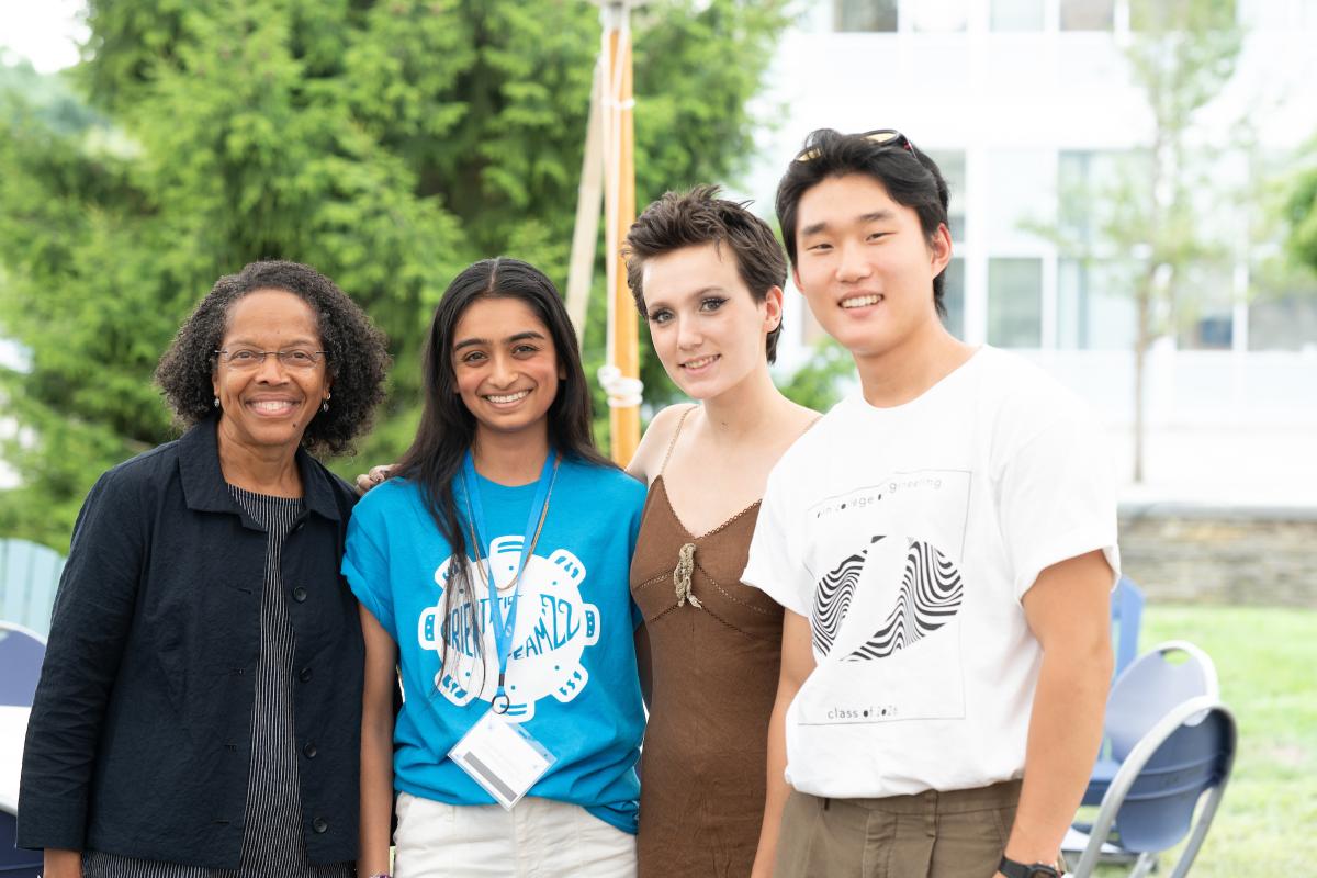 Four people stand in a line outside, all facing the camera.