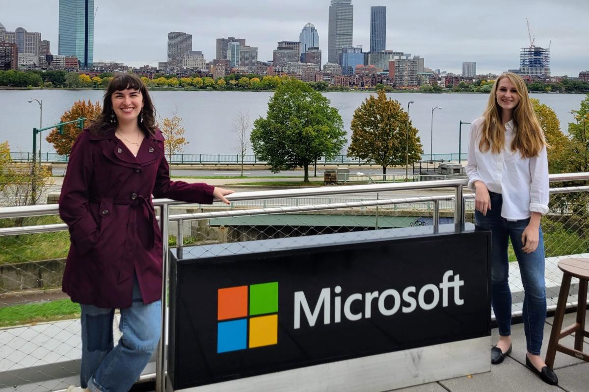 Two young women stand on opposite sides of an outside Microsoft sign.