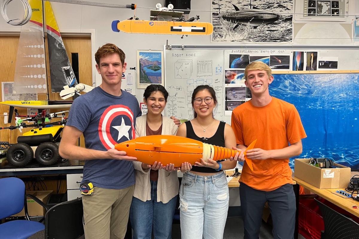 A group of four students hold an orange robotic fish