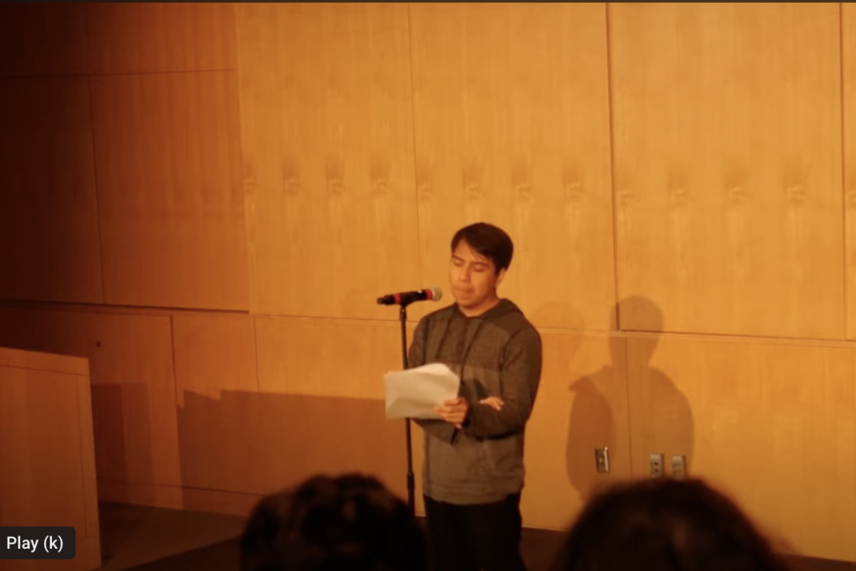 A young man standing in front of a microphone holding a piece of paper