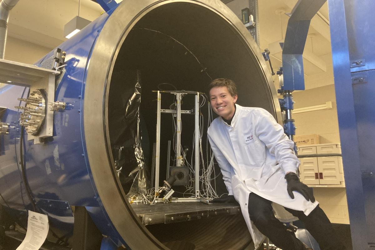 Olin student Braden Oh '23 leans against a large circular opening in the MIT Space Propulsion Lab.