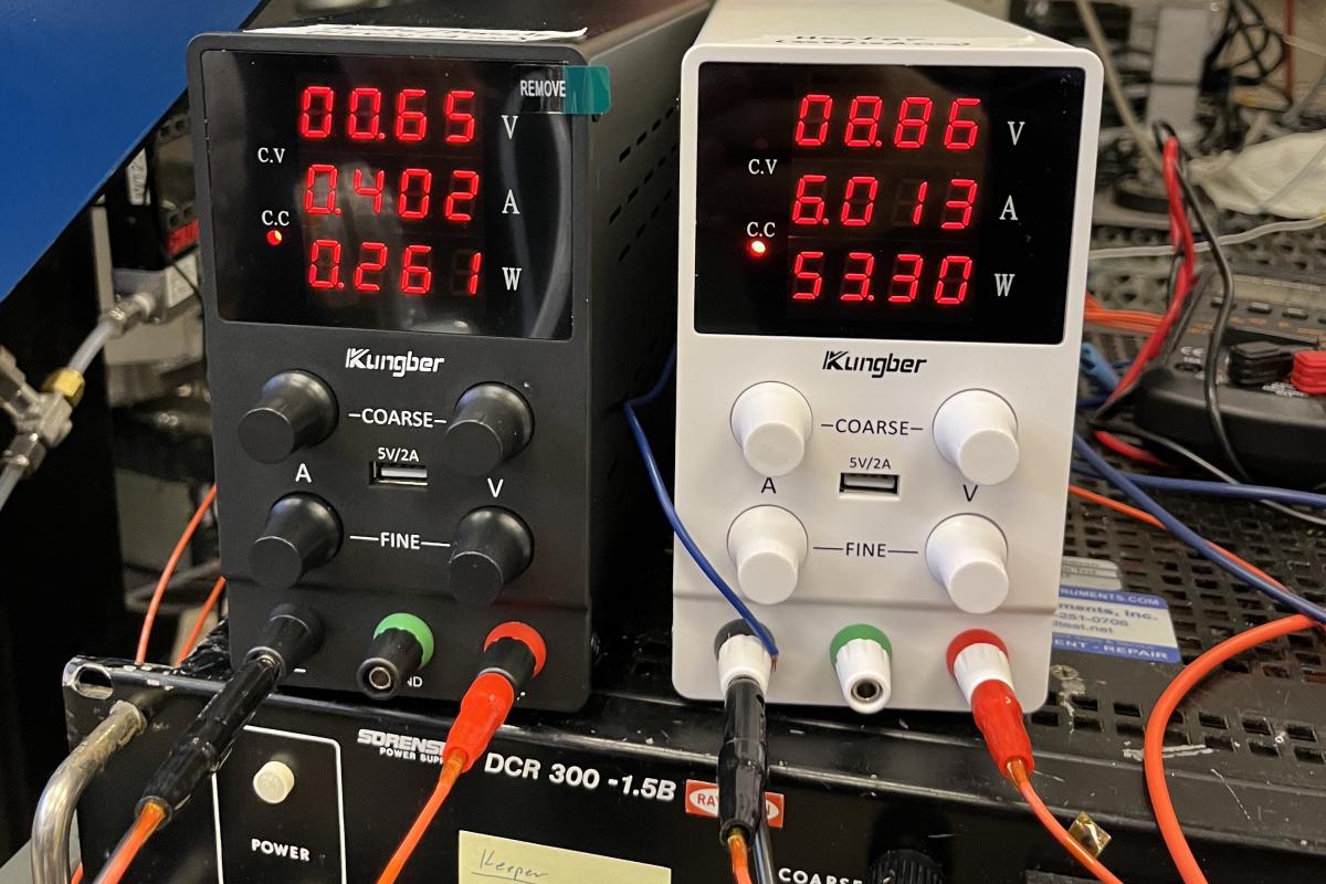 A photo of some black and white power supplies, with red digits on the screen.