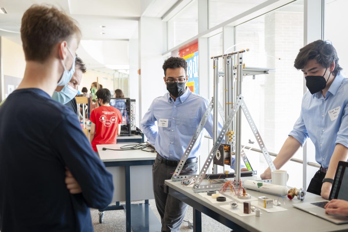 Avery Clowes ‘24 (center) and former Lab member Grant Miner ‘25 (behind table), look at the thruster while interacting with the Olin community during Spring Expo 2022. Photo by Leise Jones.   