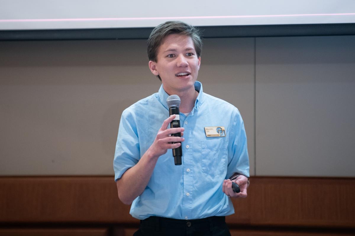 Braden Oh '23 shown with mic in hand speaking during Draper Research Symposium in 2023.