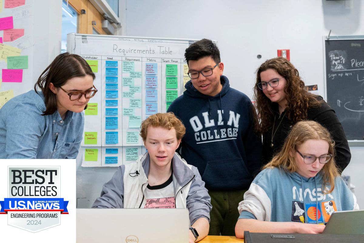 Five students work around two silver laptops in a classroom. 