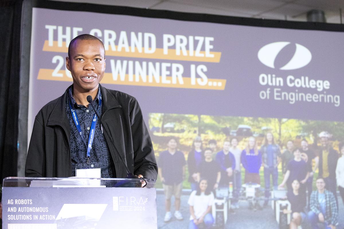 Olin College of Engineering's Kenechukwu Mbanisi, Assistant Professor of Robotics Engineering, is shown at a podium after the Olin teams wins the Farm Robotics Challenge. Olin College of Engineering's Kenechukwu Mbanisi, Assistant Professor of Robotics Engineering, is shown at a podium after the Olin teams wins the Farm Robotics Challenge.