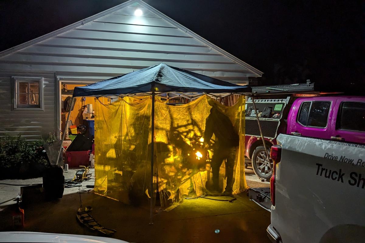 The Olin Baja team is shown working through the night in a tent. A tent with a yellow glow is shown with shadows of people from inside the tent seen on the outside.