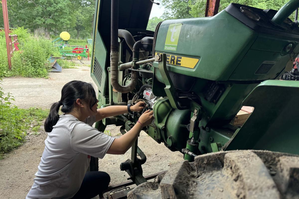 Powisset Farm Summer Research Olin student Arianne repairing the starter motor on a tractor.
