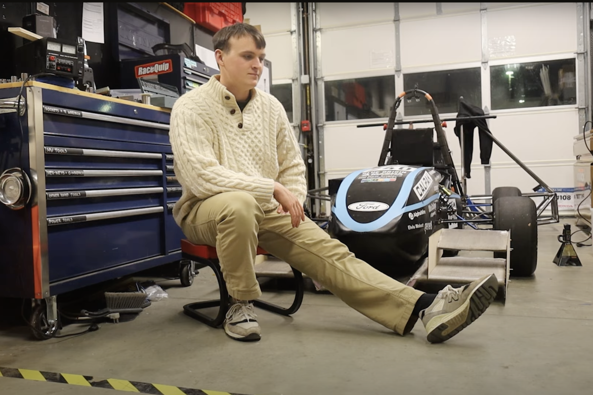 An Olin College engineering student sitting in a garage in front of a Formula SAE car.