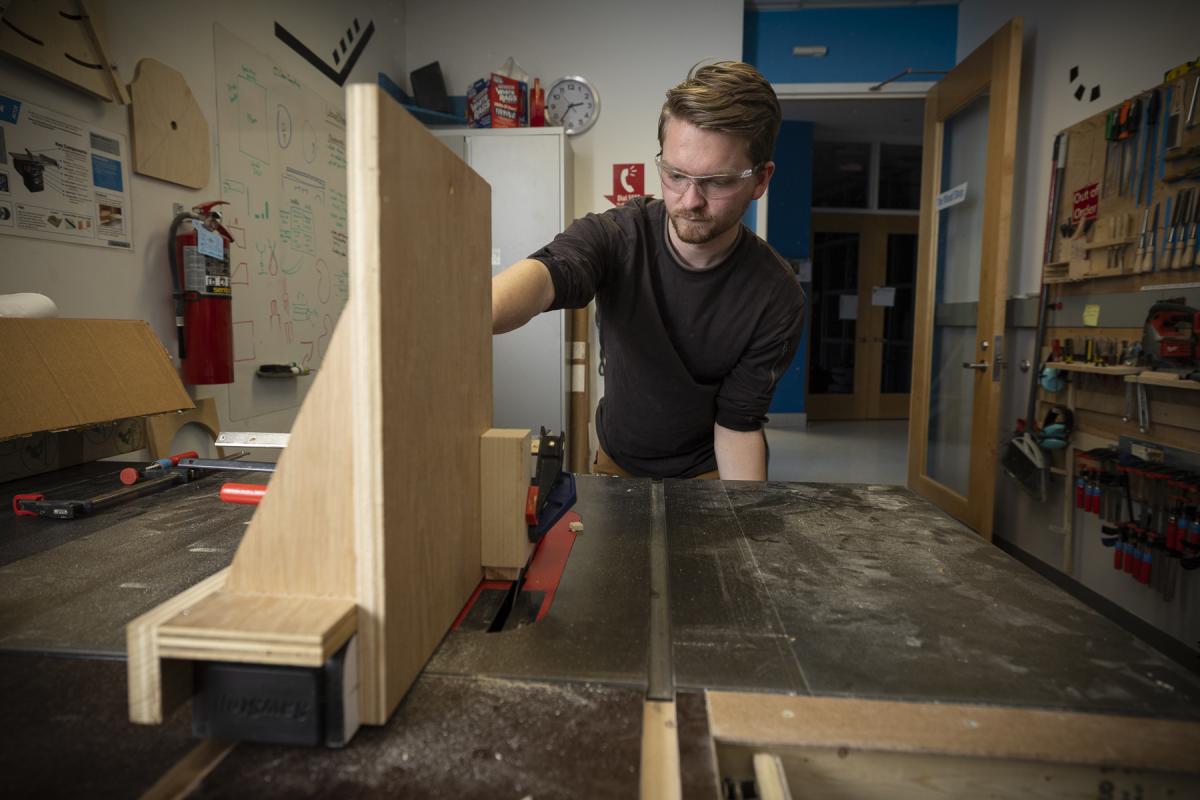 Student cuts a piece of wood on a saw machine. Student cuts a piece of wood on a saw machine.