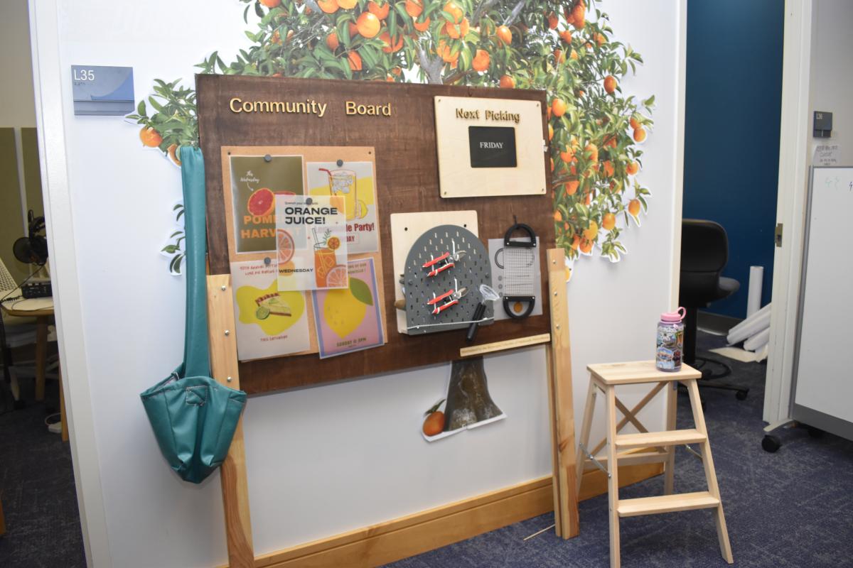 A brown board that reads "Community Board." It stands in front of an orange tree wall graphic.