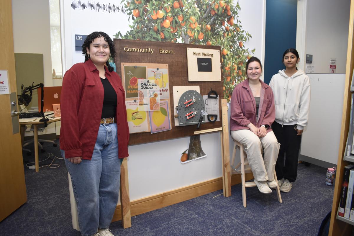 Three students stand around their final project. 