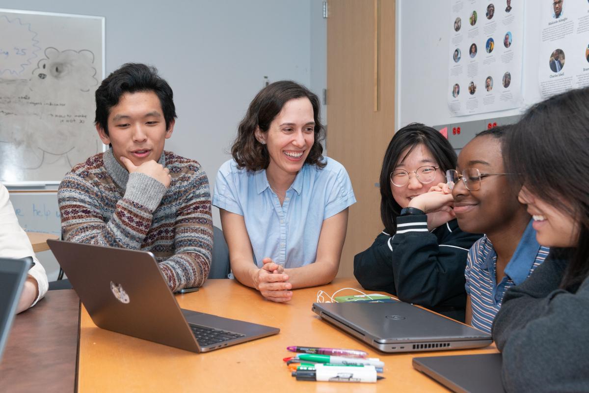 Students gather around a laptop with Andrea Cuadra ’13, Assistant Professor of Computer Science, who wears the light blue shirt.