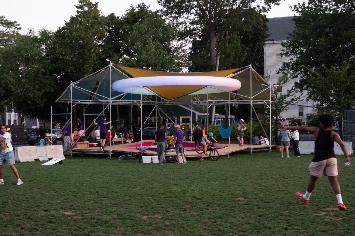A platform with covers above it held up by metal poles. The white ring lights up at night. There are people throughout the photo talking and playing ball. 