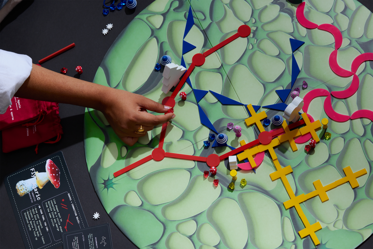 A hand is shown playing the board game "Shroomscape." A hand is shown playing the board game "Shroomscape."