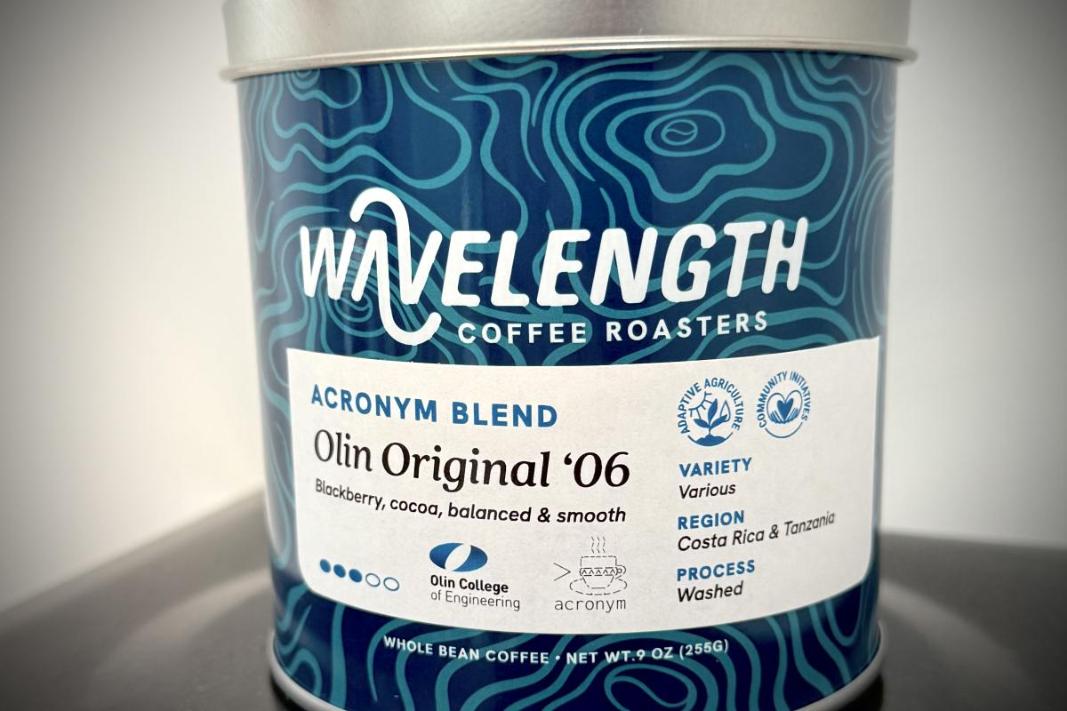 The can of coffee for ACRONYM's Wavelength collaboration. A steel coffee can with dark and light blue designs. The white text about the label reads "Wavelength Coffee Roasters." The text within the label reads: "ACRONYM BLEND; Olin Original ’06; Blackberry, cocoa, balanced & smooth," and to the right of that text it reads: "Variety: Various; Region: Costa Rica & Tanzania; Process: Washed."