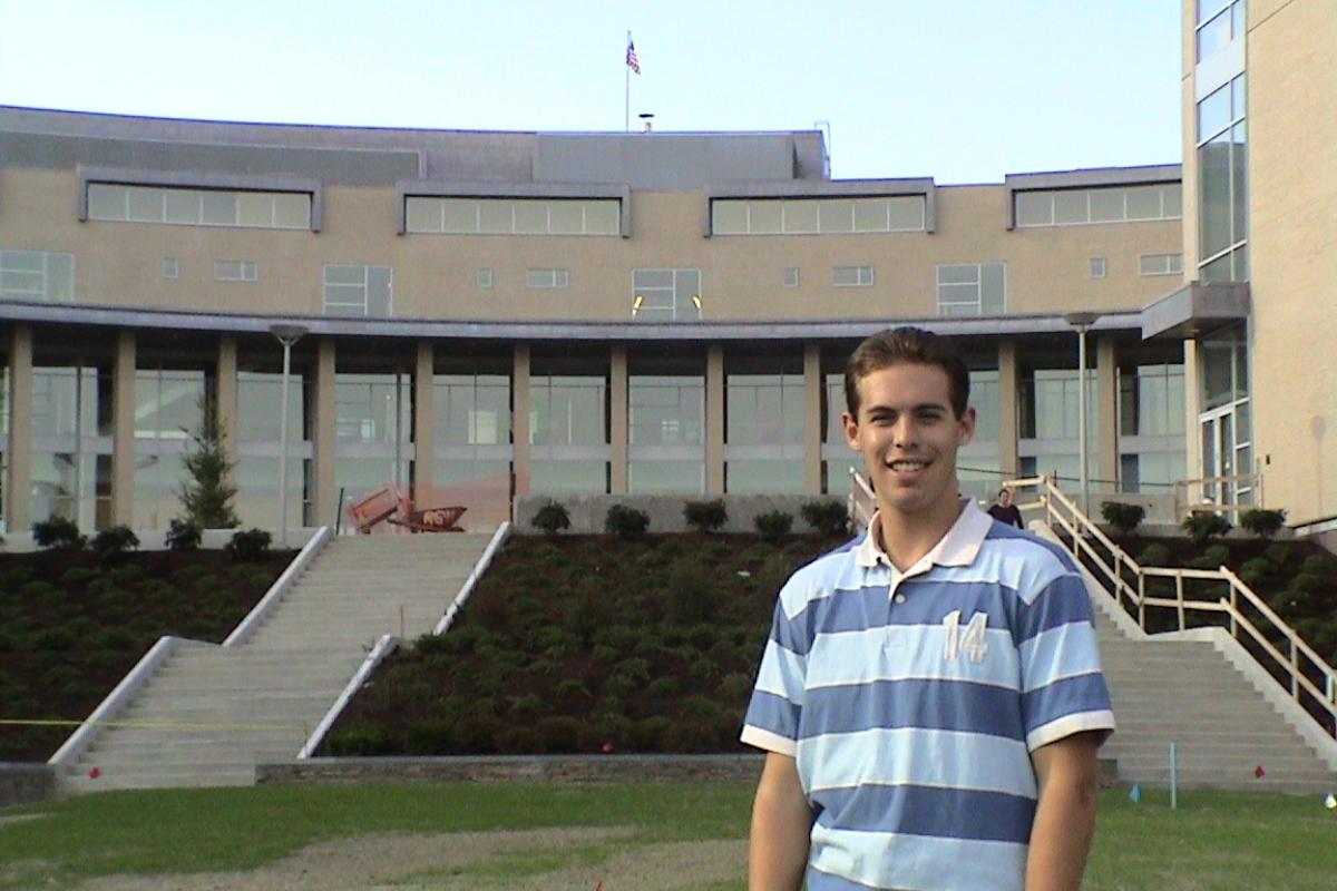 Kevin Tostado ’06 stands on the Great Lawn with the MAC behind him.