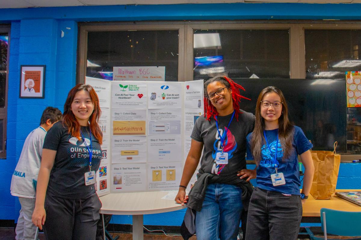 Three students stand in front of their trifold poster board presentation. 