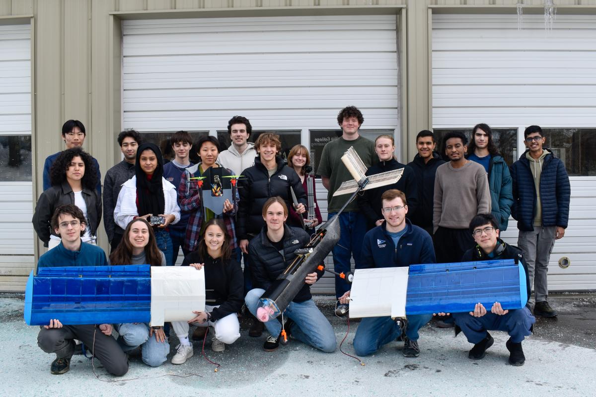 The Olin AERO team poses in two rows in front of the LPB. Several students are holding project components.