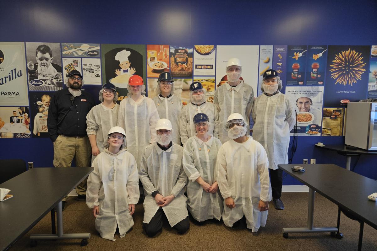 A group of students and staff stand in the Barilla office wearing personal protective gear. 