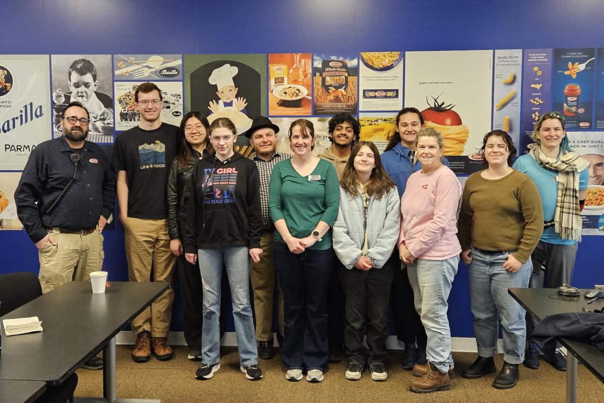 Students and staff stand in front of a blue wall with Barilla advertising posters. 