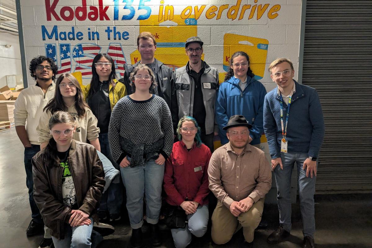 A group of students and staff stand in front of a mural at Kodak. 