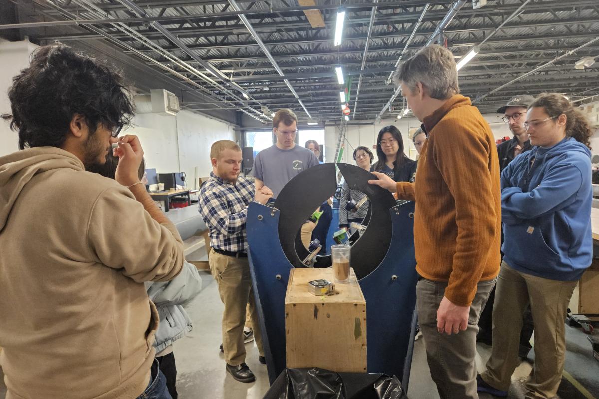 Students and staff stand around an object being manufactured at The Moore Brothers Company facility. 